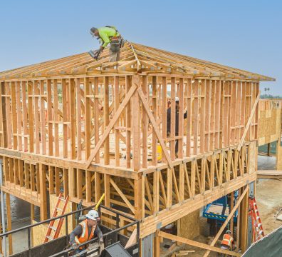 A house under construction, featuring a wooden frame with visible beams and studs.