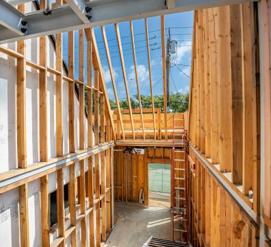 Construction site with a partially built house featuring exposed wooden beams and studs.