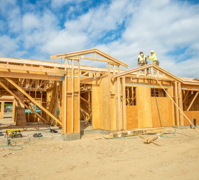Wooden house framing in progress, with beams and studs forming the structure.