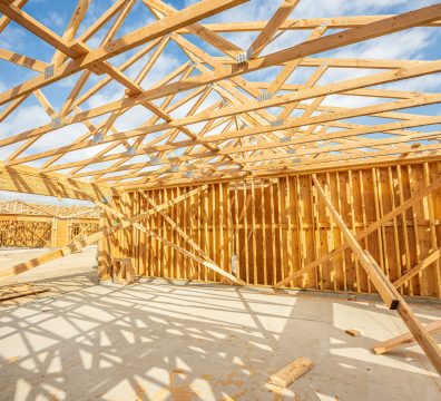 An under-construction house with a wooden frame, displaying structural beams and studs.