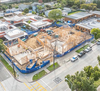 Aerial view of a wood framing construction site, showcasing wooden structural framing, construction workers, and surrounding buildings. Captured in a busy urban area.