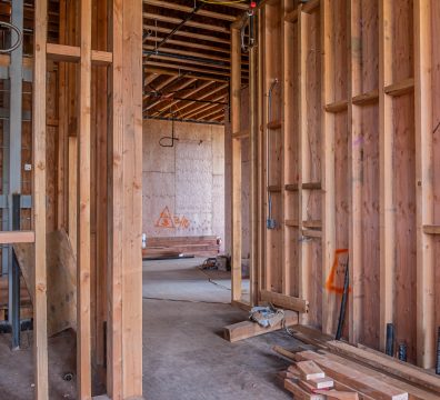 Partially constructed house with a wooden frame, featuring walls and roof structure.
