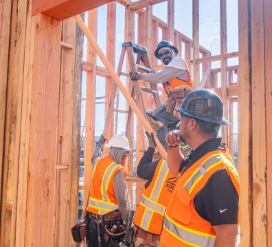 A wooden house frame with exposed beams and studs, showing progress in construction.