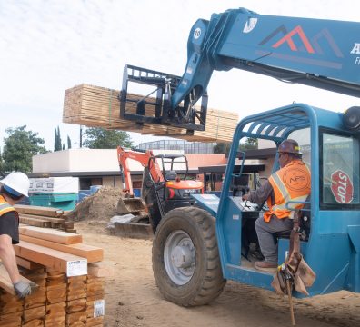 Image of a construction site vehicle lifting wood frames