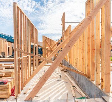 A wooden house frame under construction, featuring visible beams and studs creating the walls and roof.
