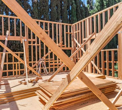 Framing interior of a wood-framed home with cross bracing and plywood sheets stacked on the floor