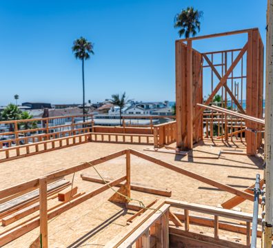Exposed second-story stick framing with ocean view and palm trees in the background